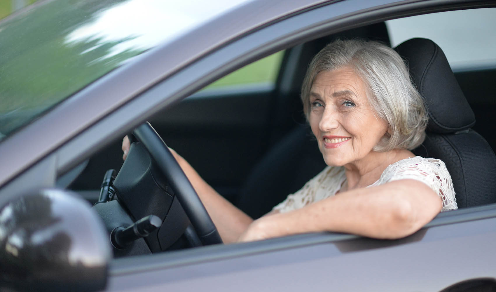 Glückliche ältere Dame freut sich am Steuer über ihr Gebrauchtfahrzeug von ENPA Automobile